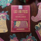 East End Press Garland packaging on a wooden surface with decorative paper pieces.
