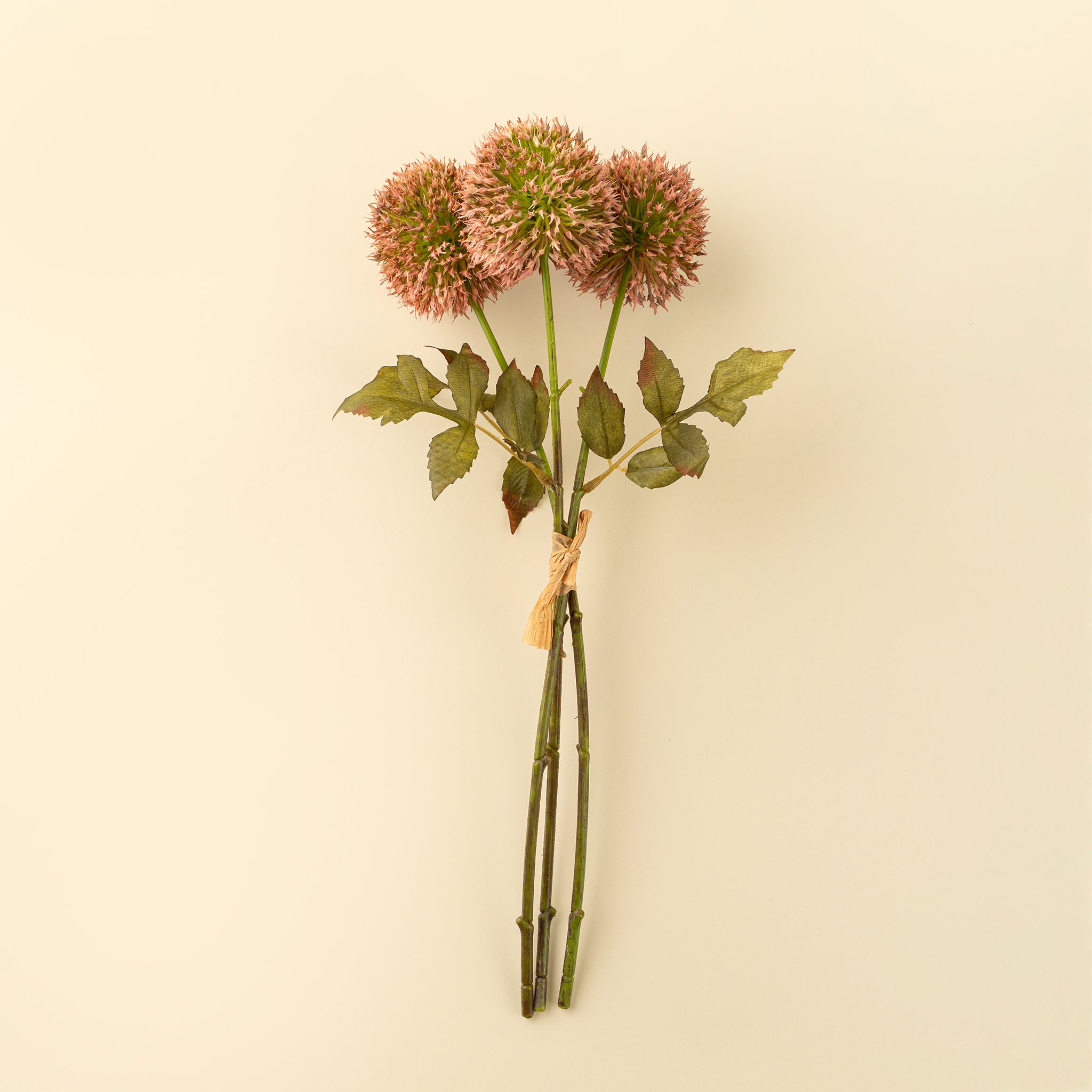 Artificial flower arrangement with pink allium flowers with green stems on a beige background