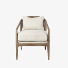 Armchair with light brown stain and sloped arms and cane back and light beige cushions on a white background