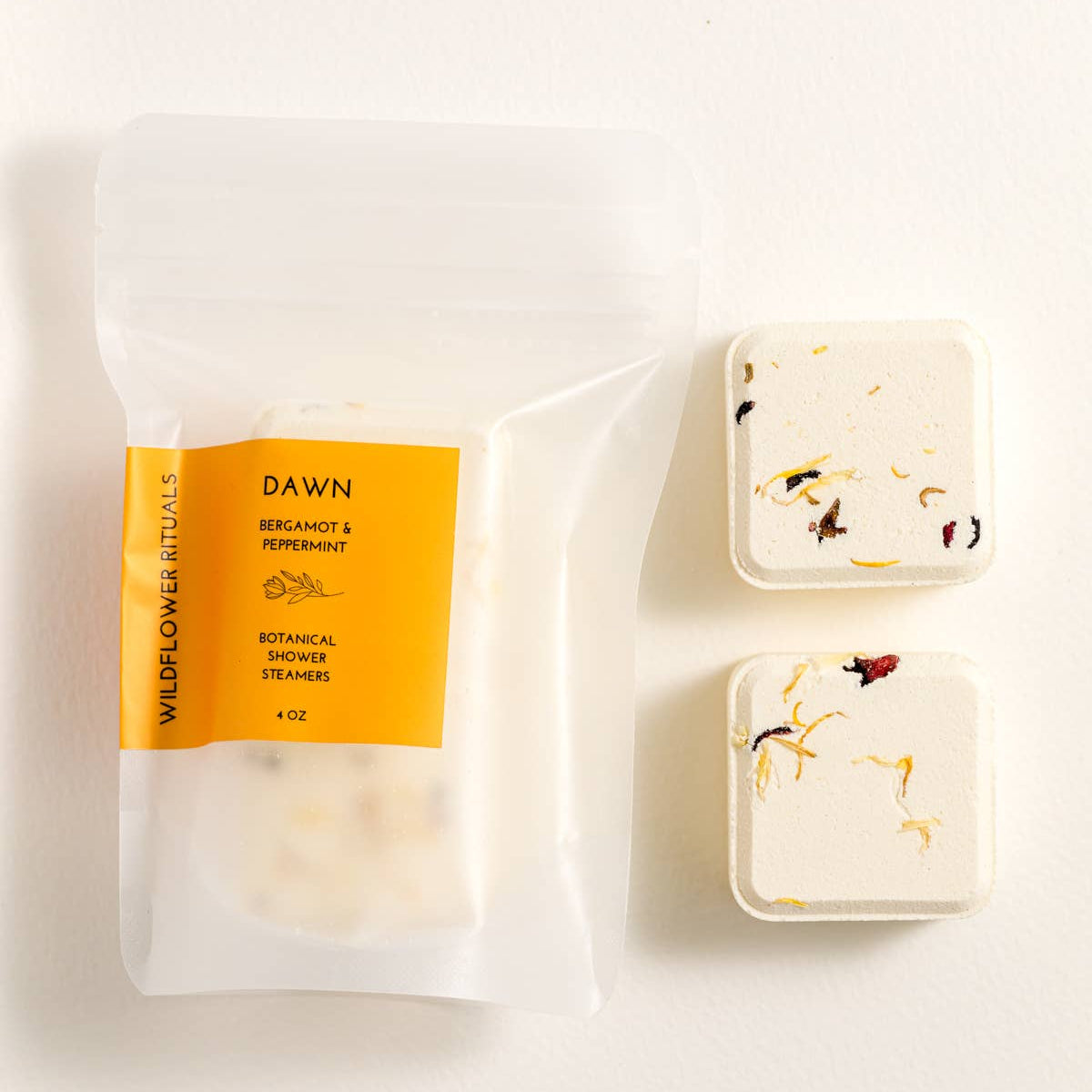 Two square shower steamers next to a clear package with a yellow label.