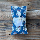 A blue floral eye pillow wrapped with a cream ribbon and a paper tag reading 'BELLE'S FRENCH YUKE', placed on a rustic wooden plank surface.