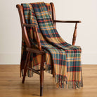 Plaid blanket draped over a wooden chair on a wooden floor.