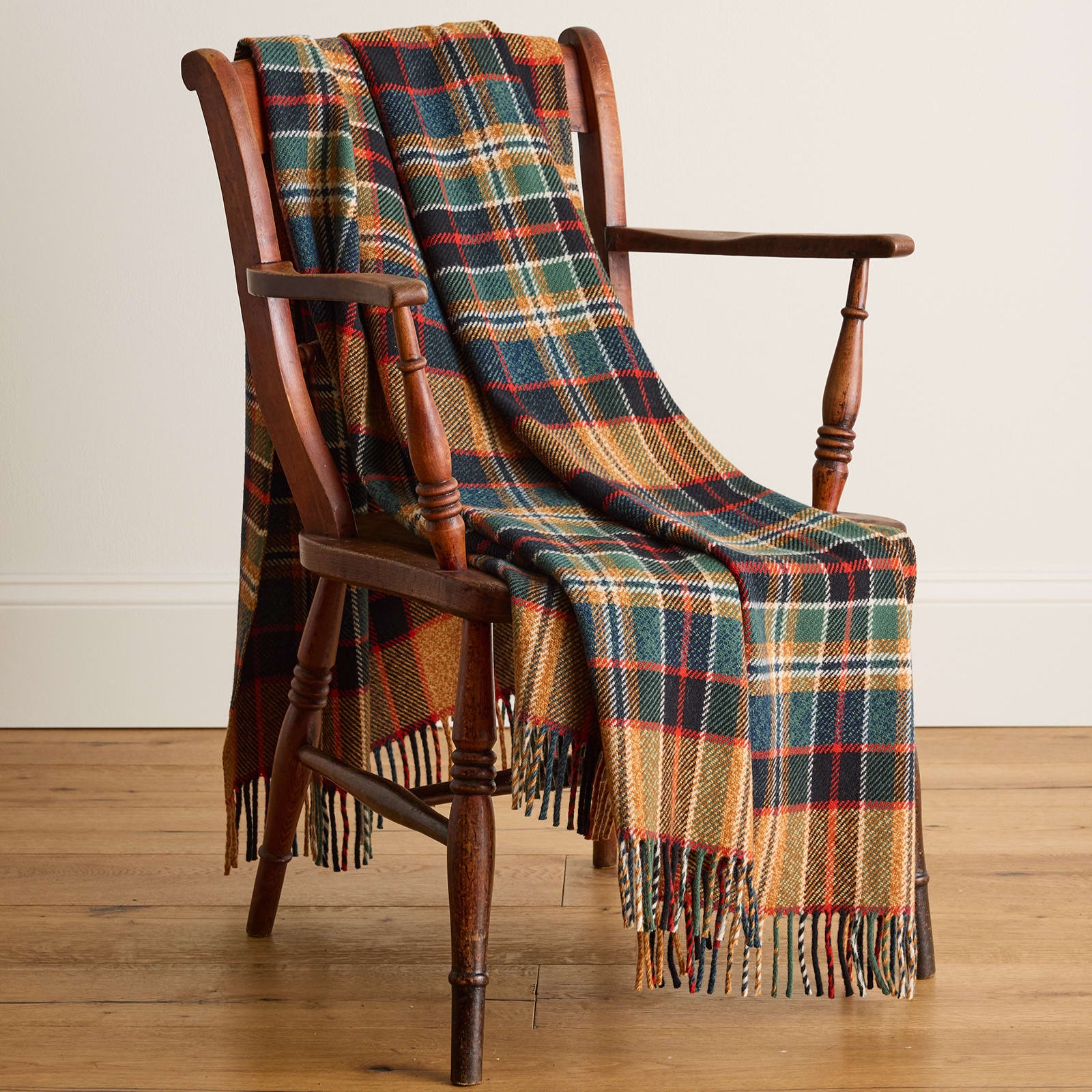 Plaid blanket draped over a wooden chair on a wooden floor.
