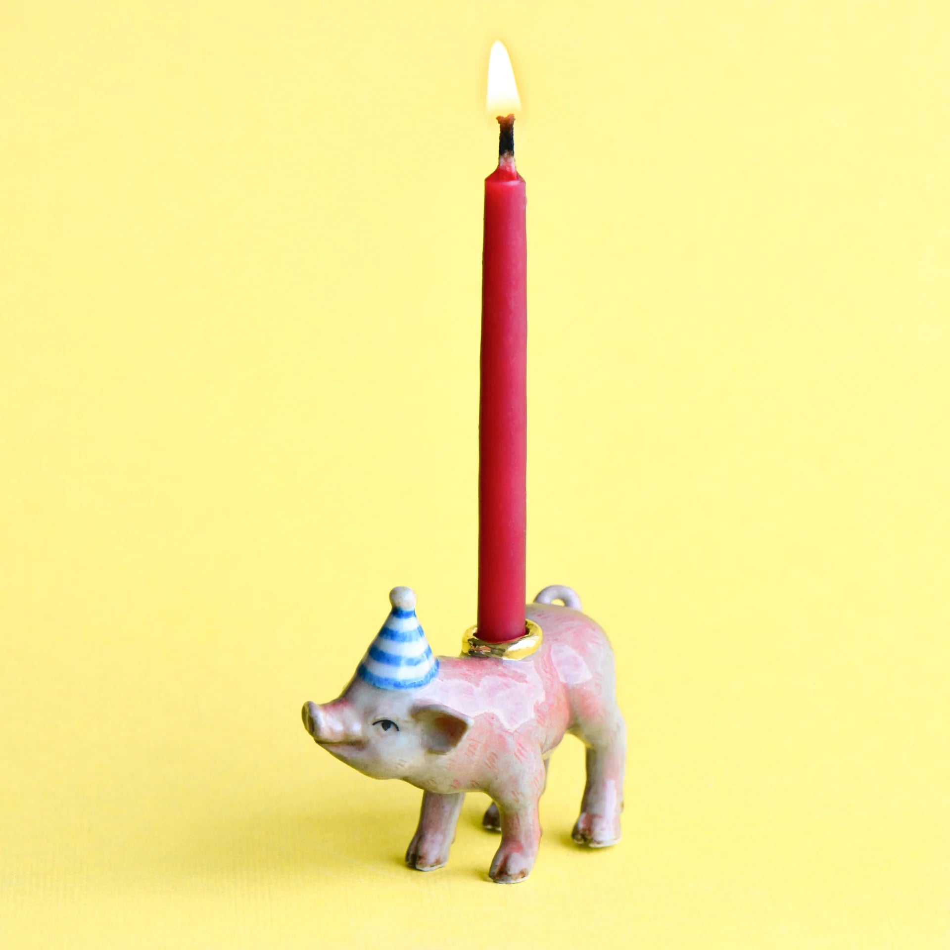 Pig-shaped candle holder with a lit red candle on a yellow background