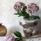 Decorative vase with pink flowers and green leaves on a textured surface
