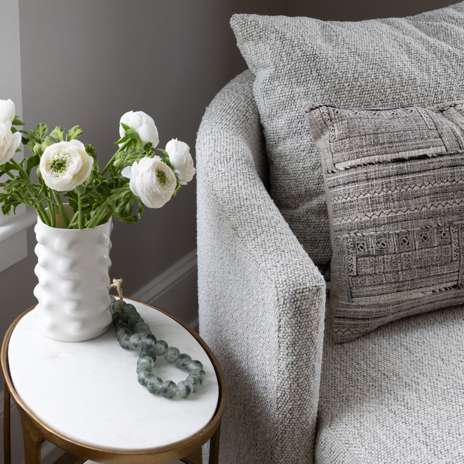 Close up of Four hands brand Farrah chaise with small marble side table and flowers