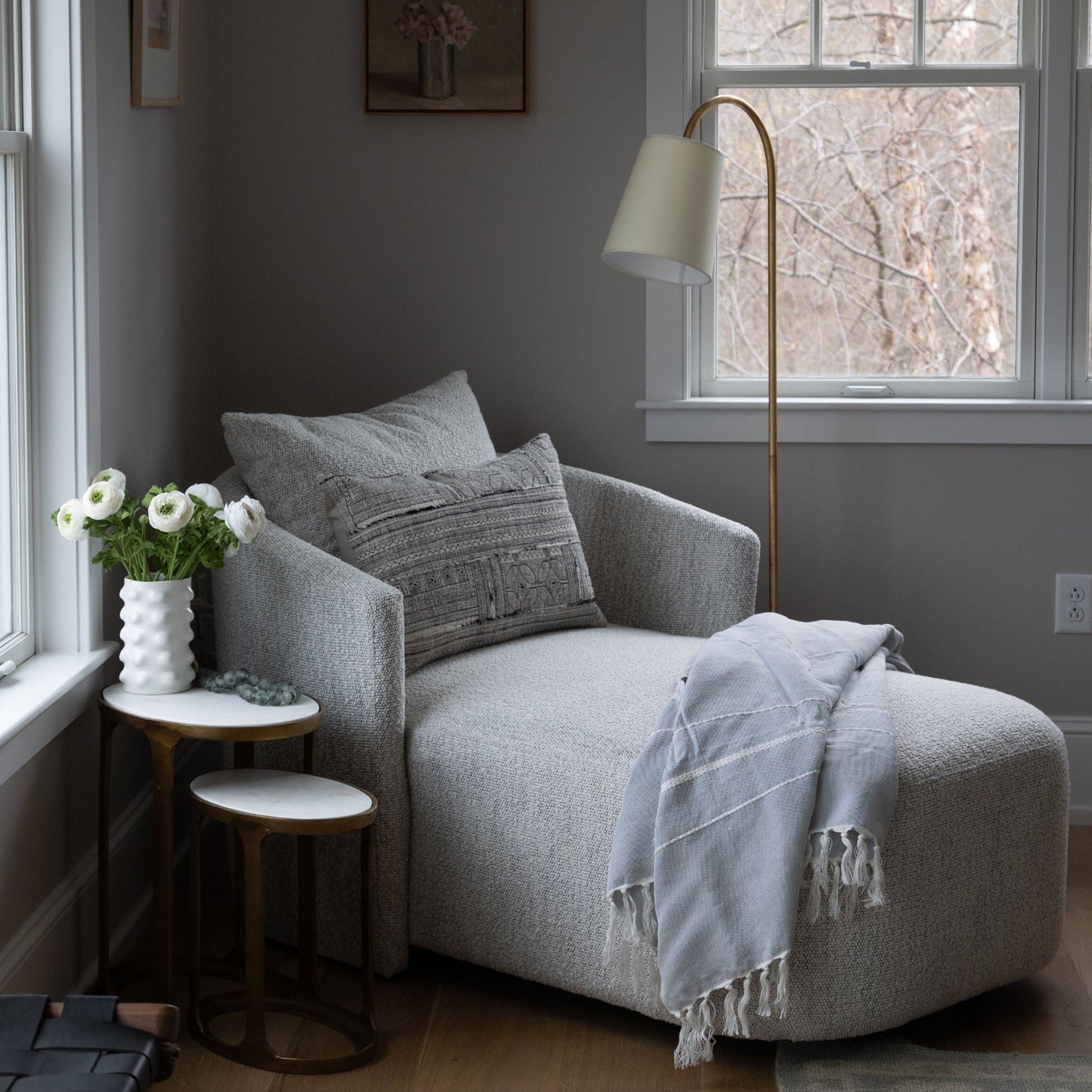 Four hands brand Farrah chaise in a bedroom by a window next to a table with flowers