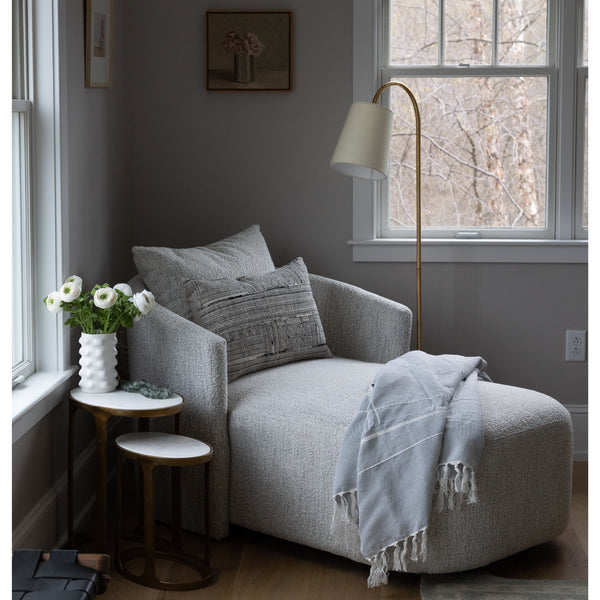 Four hands brand Farrah chaise in a bedroom by a window next to a table with flowers
