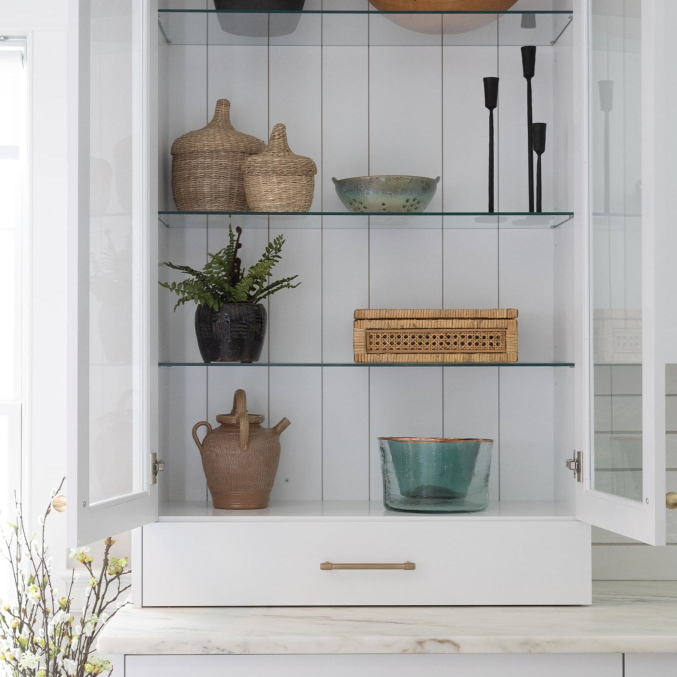 White kitchen cabinet with glass doors open to shelves decorated with wood bowls and kitchen accessories 