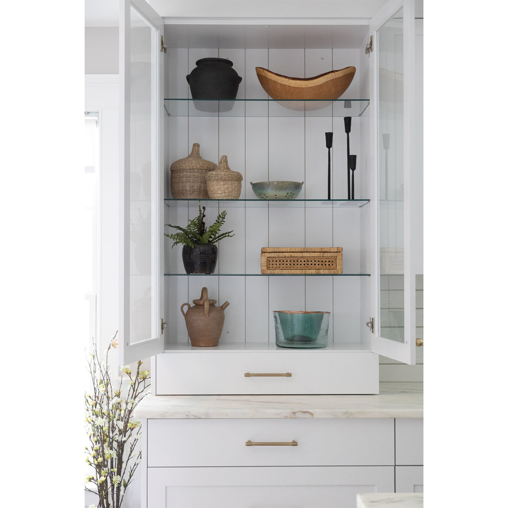 White kitchen cabinet with glass doors open to shelves decorated with wood bowls and kitchen accessories 