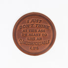 'An Uncomfortable Life' Leather Coaster on a white background at Addison West