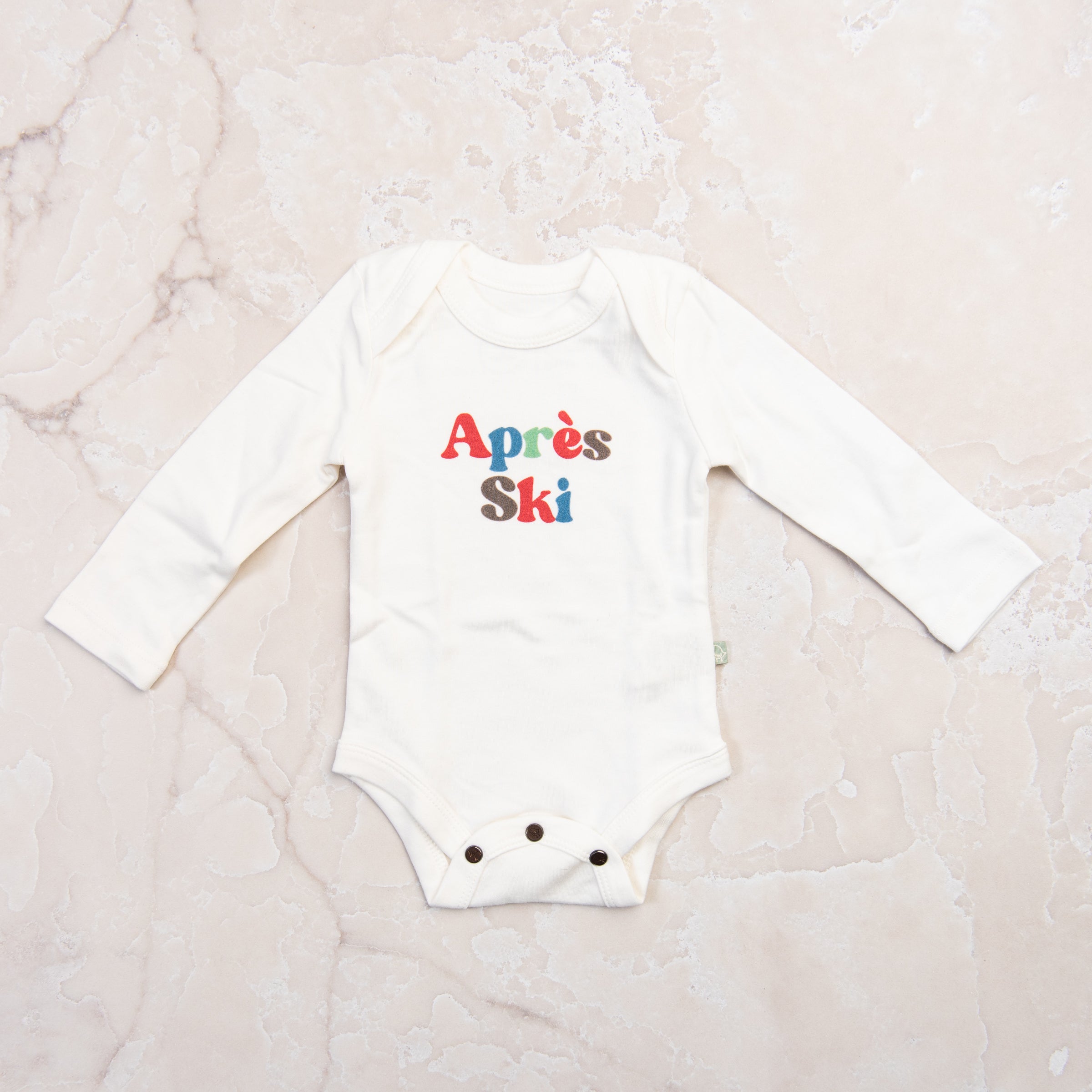 Apres Ski Baby Organic Cotton Bodysuit on a marble table at Addison West