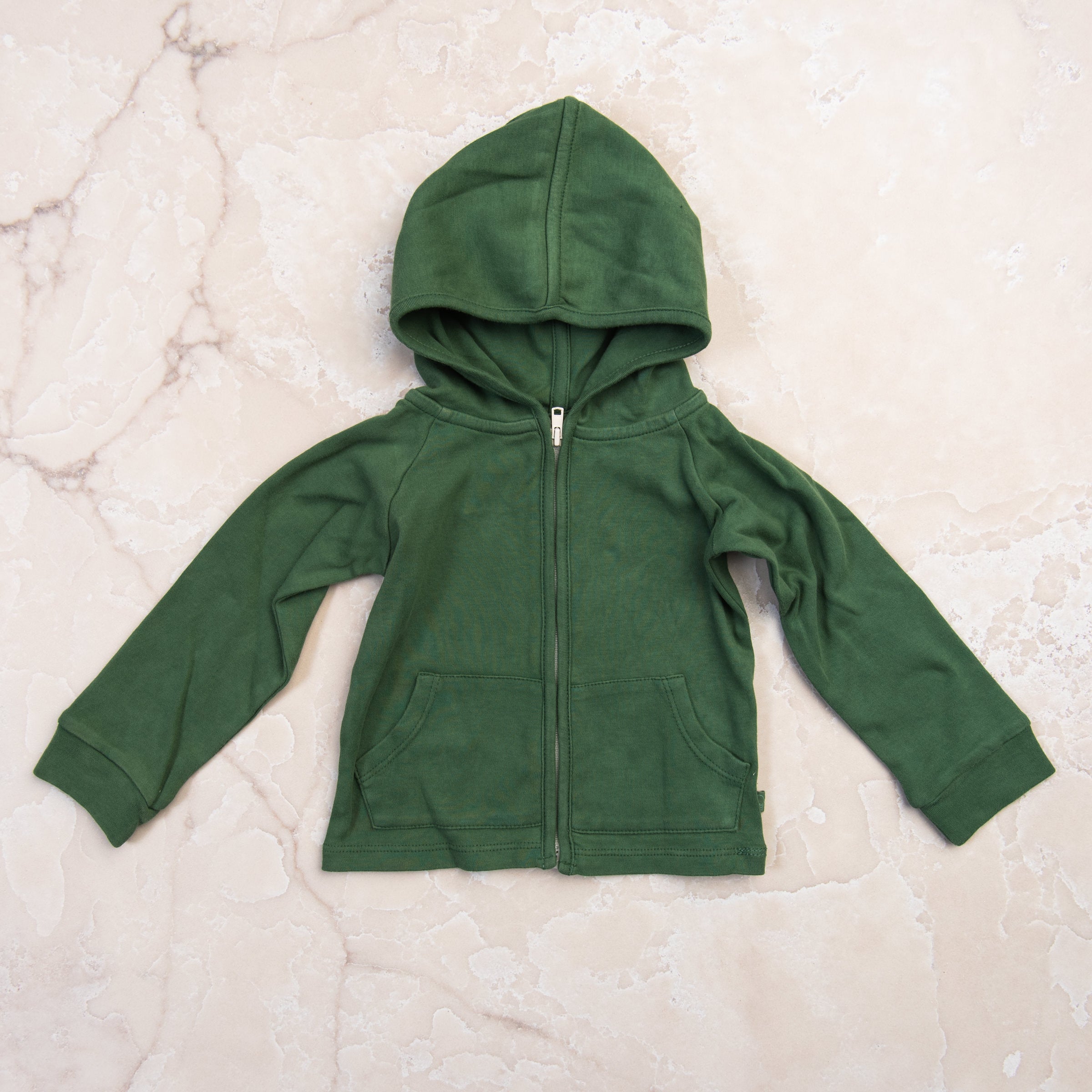 Organic Hoodie in Basil Green on a marble table at Addison West