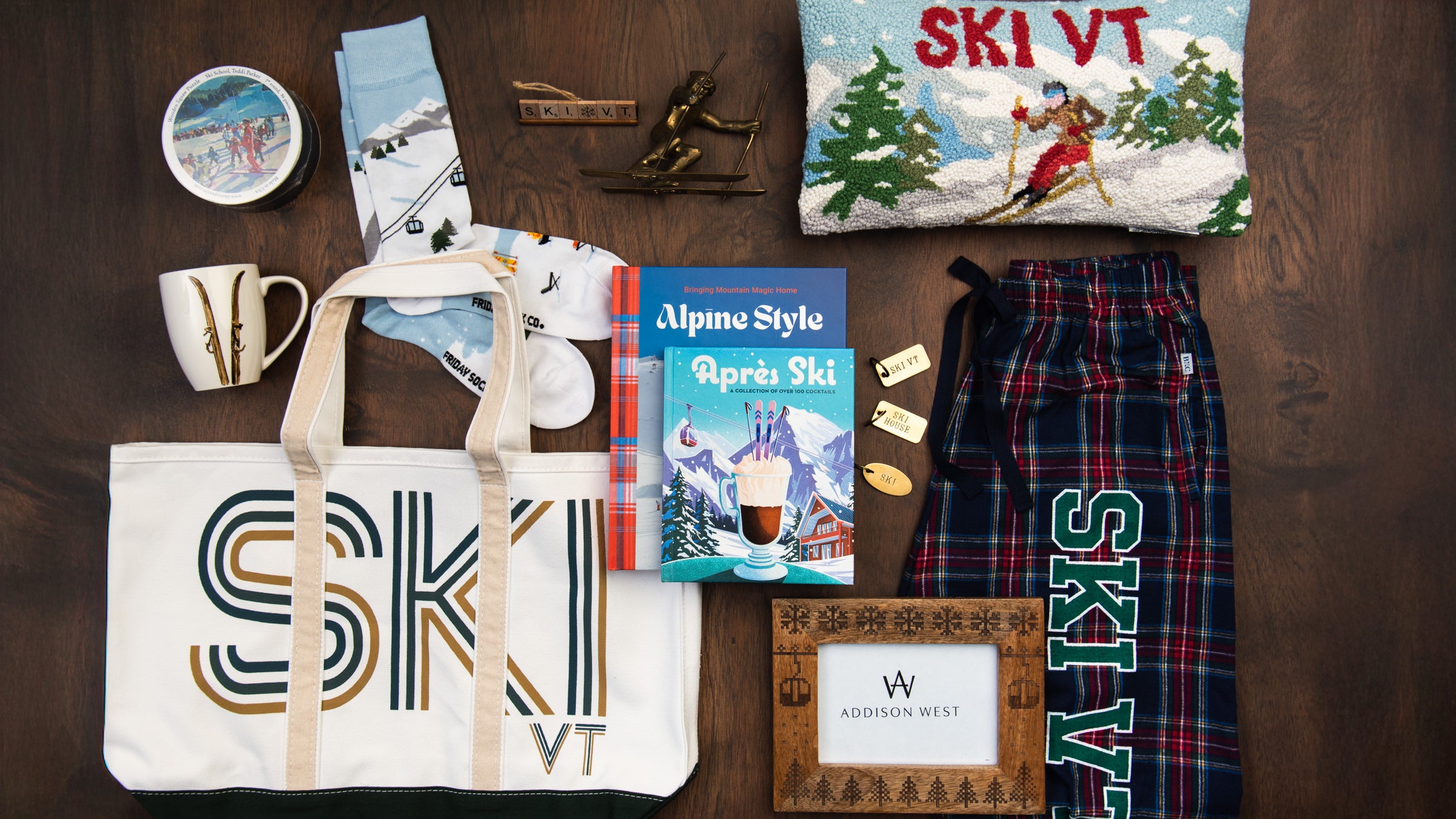Collection of Ski things, ski vt flannel pants, ski vt embroidered pillow, ski vt tote bag, ski mug, ski socks, ski books on a wood table at Addison West