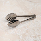 Scalloped Serving Tongs on a beige background at Addison West