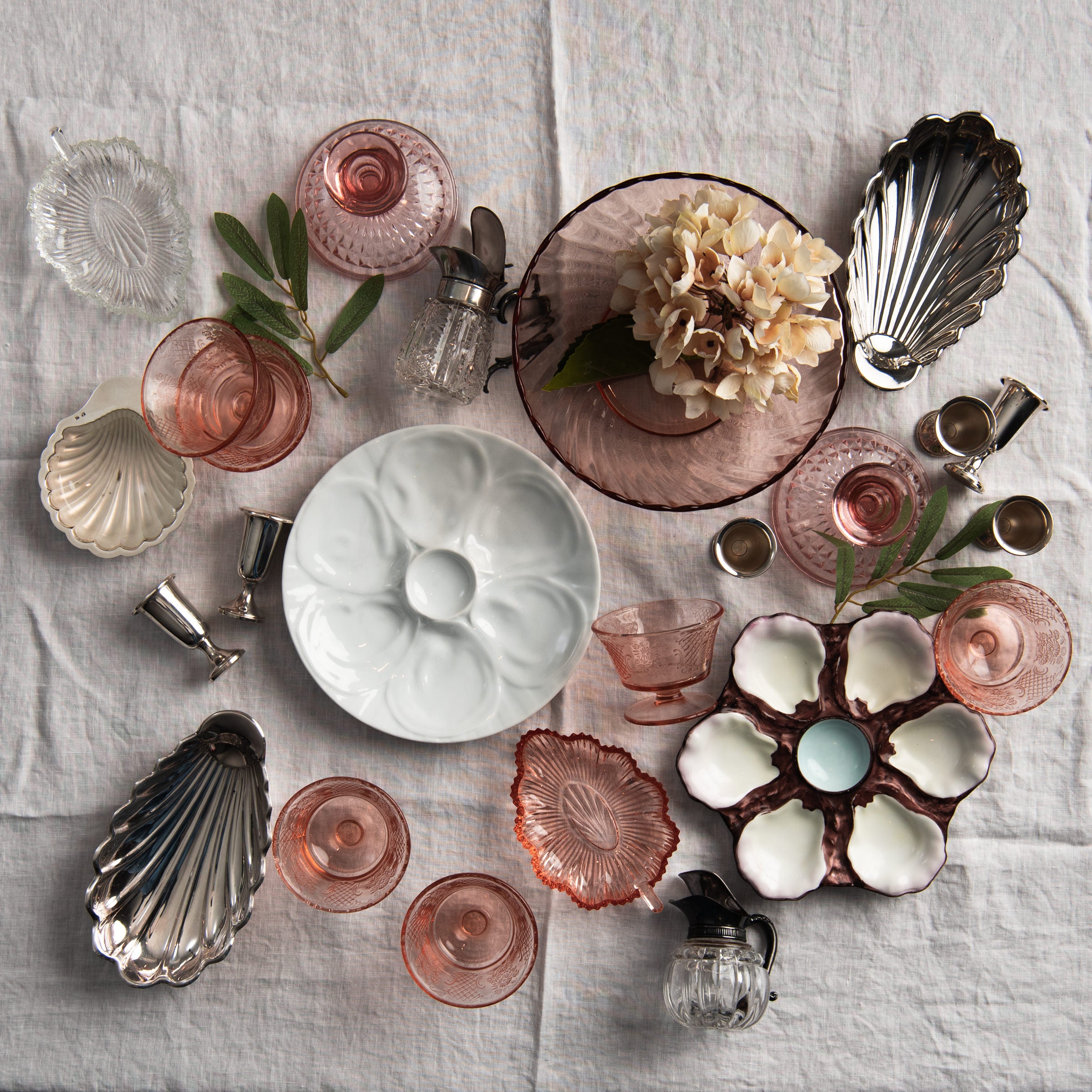 Vintage collection of blush pink glassware, silver shell trays, oyster plates, maple syrup pitchers on a white linen table at Addison West