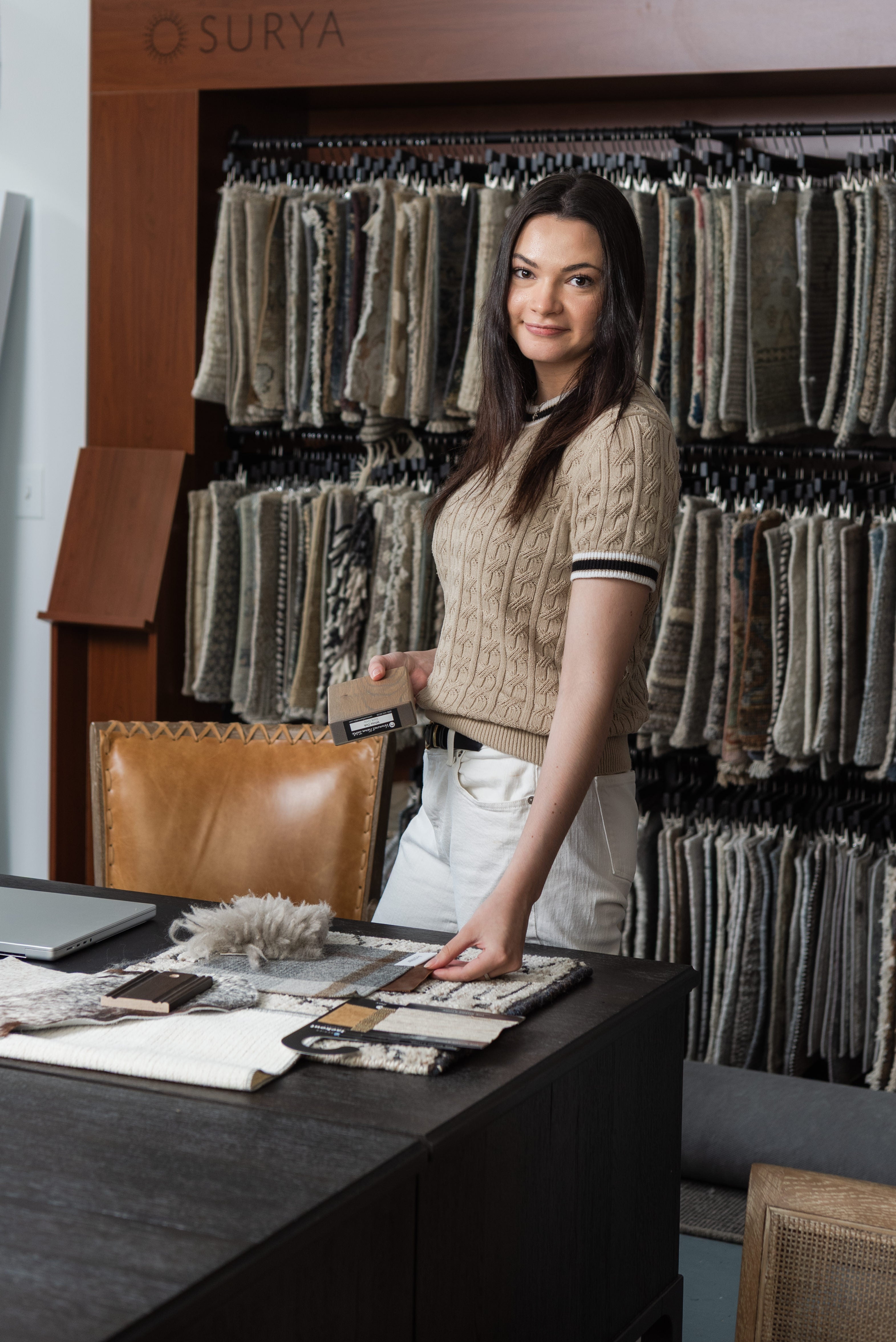A woman standing at a dark desk with interior design samples around her.
