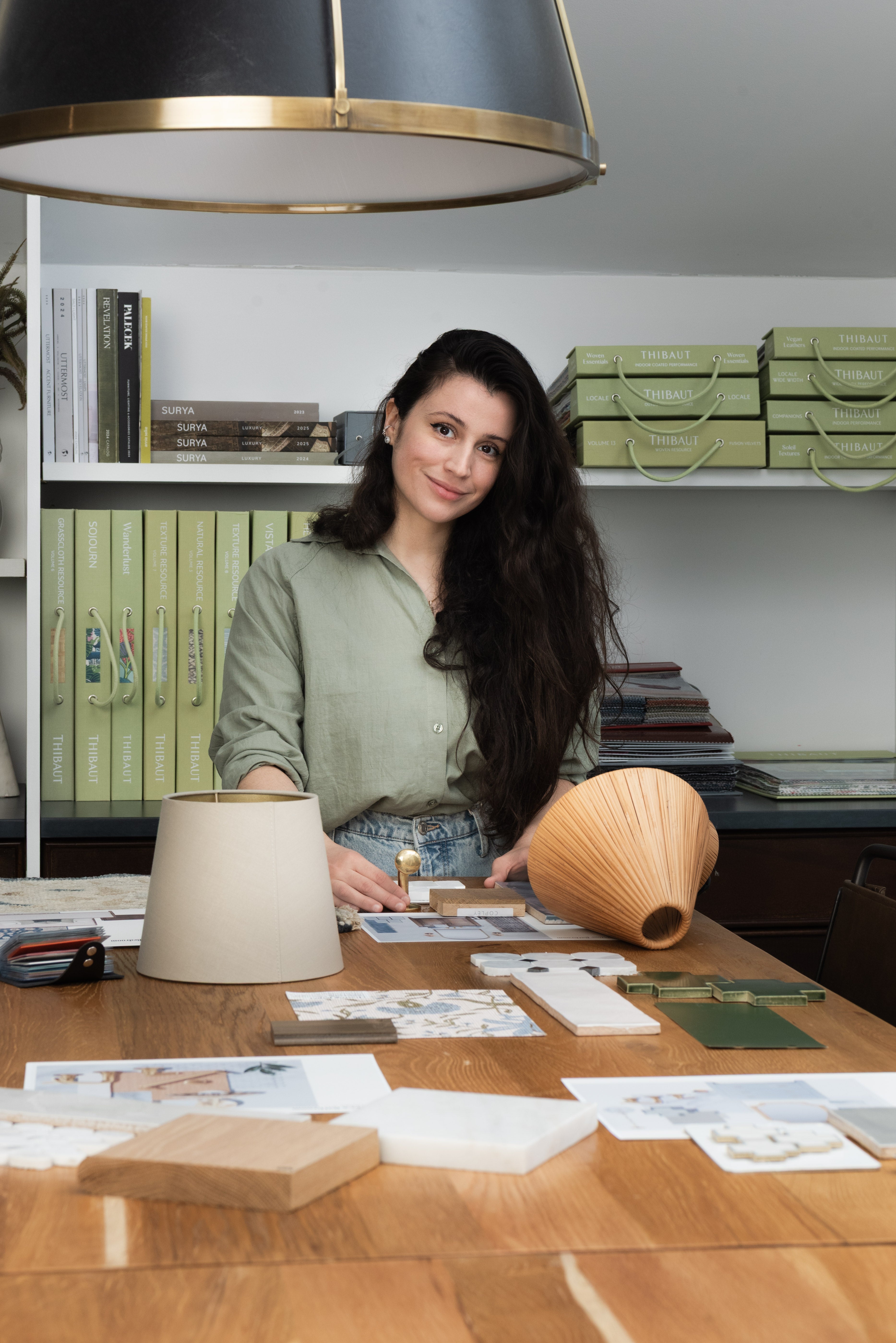 A woman standing at a desk smiling at the camera with interior design samples around her.