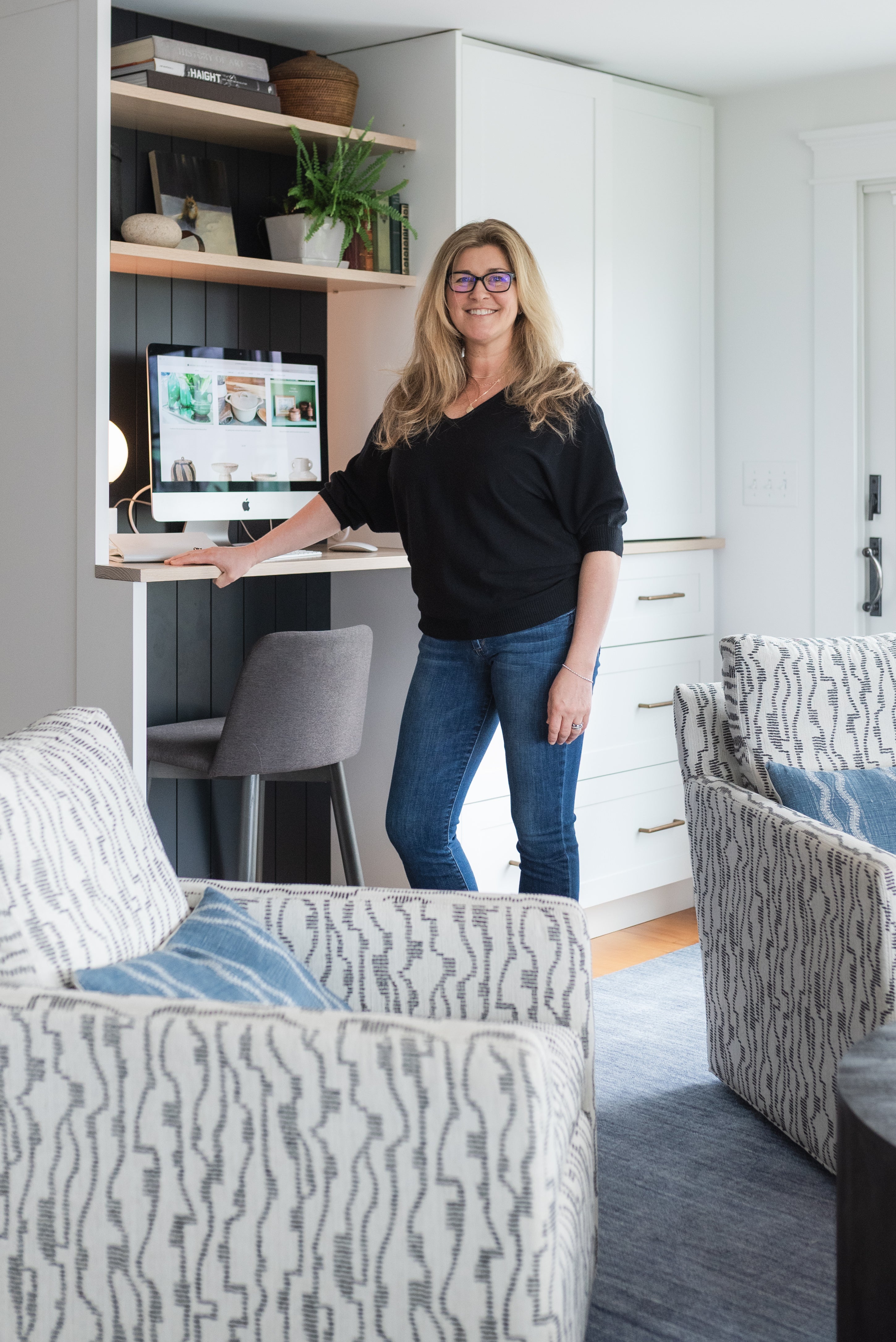 Woman standing in a modern living room with a desk and computer.
