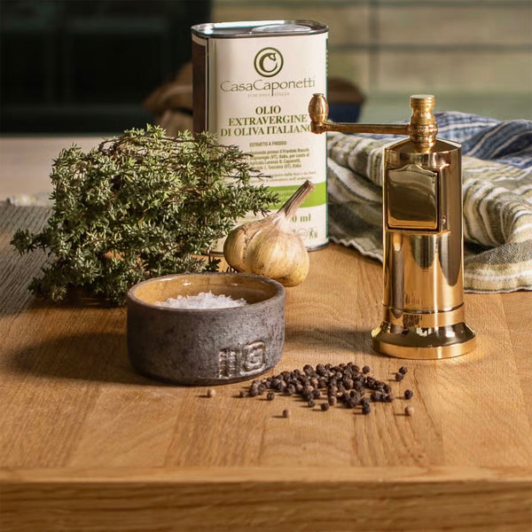 Brass Alexander Chefs' Mate Pepper Grinder on a wood surface with herbs and olive oil
