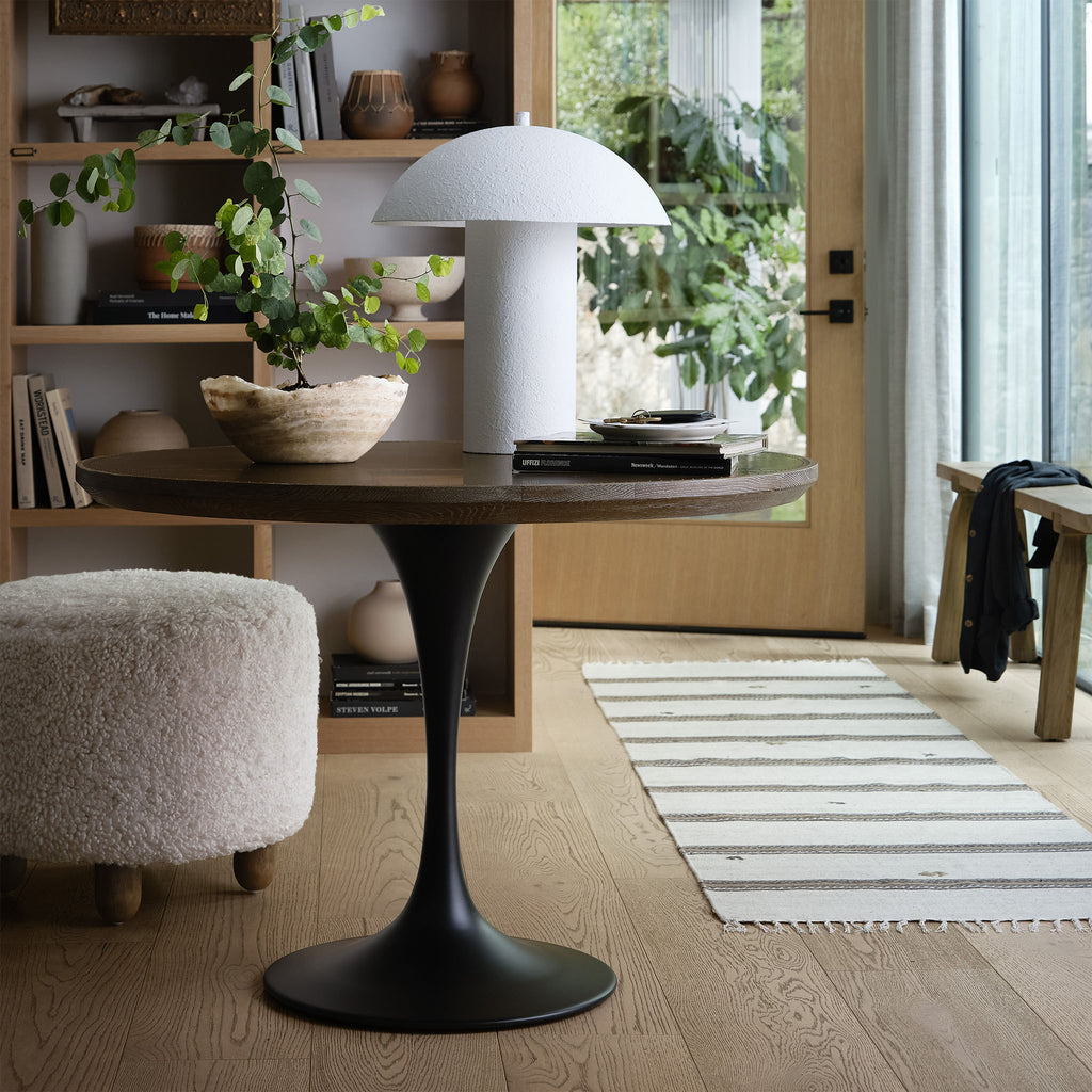 Four hands brand Aniston ottoman in natural shearling style upholstery in a room with a round table and wood floor and plants