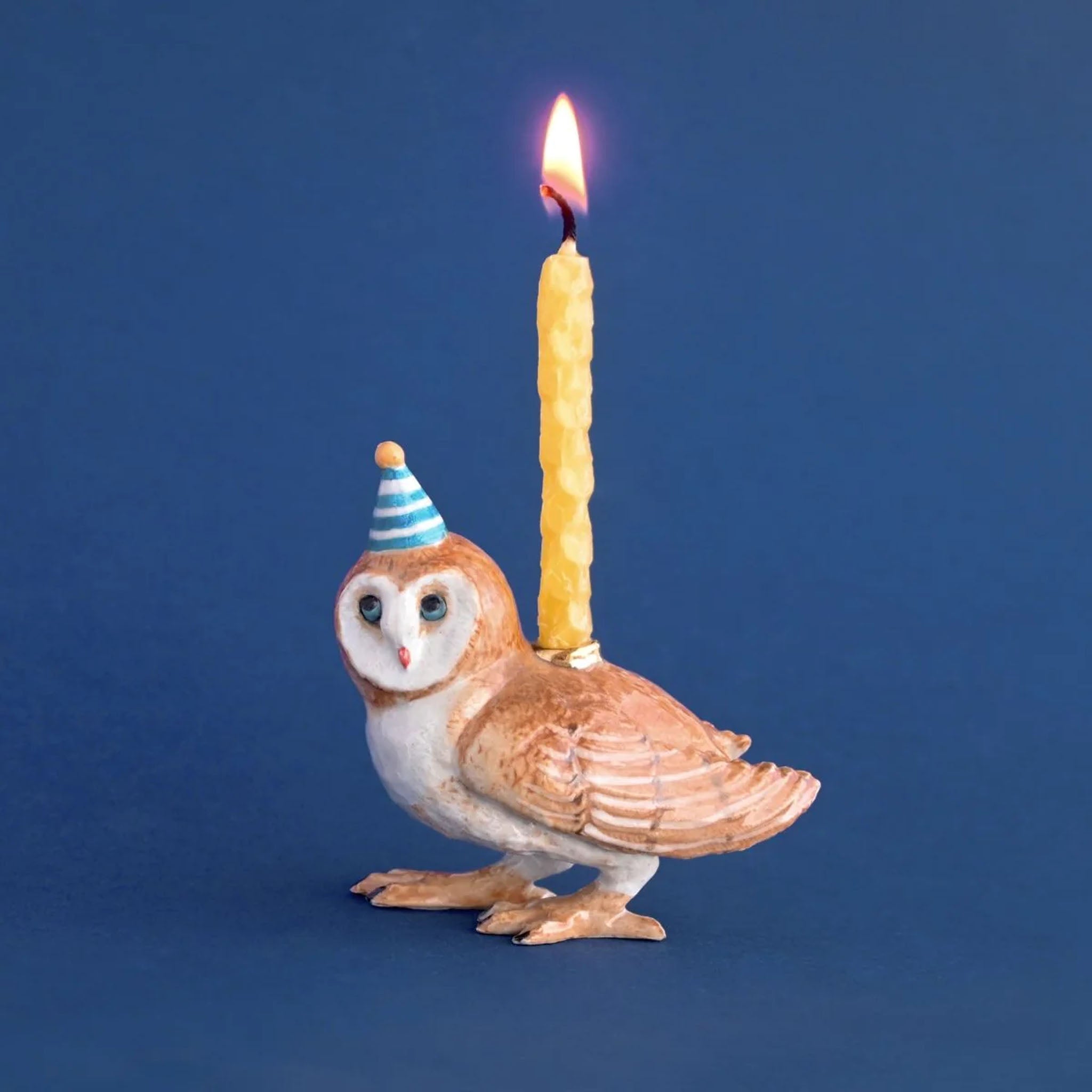 Owl-shaped candle holder with a lit candle on a blue background
