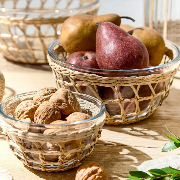Three rattan wrapped glass bowls on wood table with nuts and pears inside