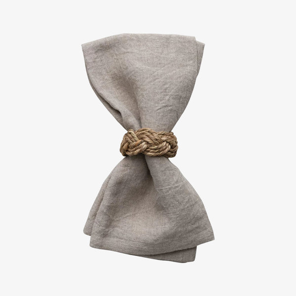 Beige linen napkin with seagrass braided napkin ring on a white background