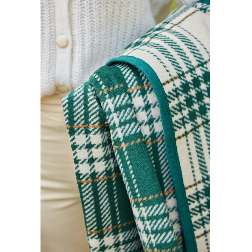 Chappy Wrap Autumn Plaid Evergreen Blanket held by a woman wearing beige pants and a creme sweater