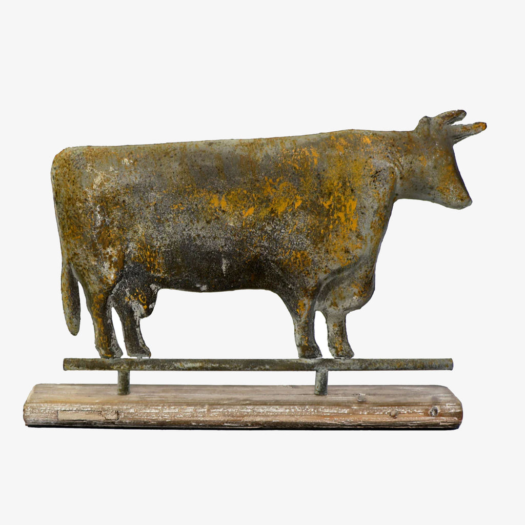 Metal cow weathervane statue on a sold wood base on a white background