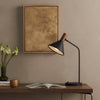 Four Hands Cullen Task Lamp in Black Leather on a wood table in a living space with tan walls and neutral painting