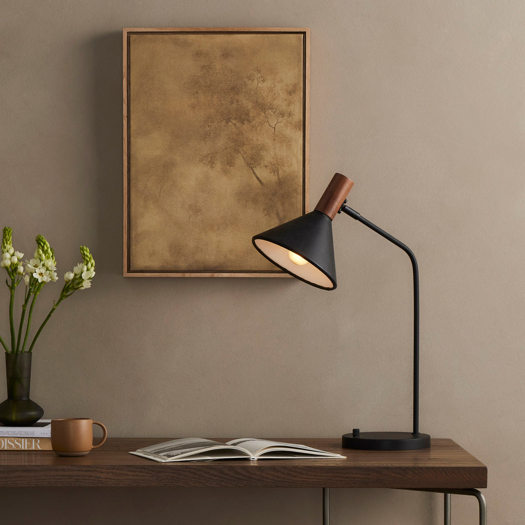 Four Hands Cullen Task Lamp in Black Leather on a wood table in a living space with tan walls and neutral painting