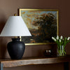 Surya brand black Dalle lamp with flared shade on a wood console with autumnal painting and vase of tulips