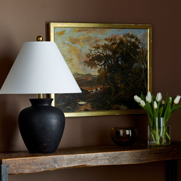 Surya brand black Dalle lamp with flared shade on a wood console with autumnal painting and vase of tulips