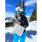 Women in ski gear on a winter mountain holding Dancing Skiers + Goggles Medium Pack