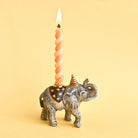 Elephant-shaped candle holder with a spiral candle on a yellow background