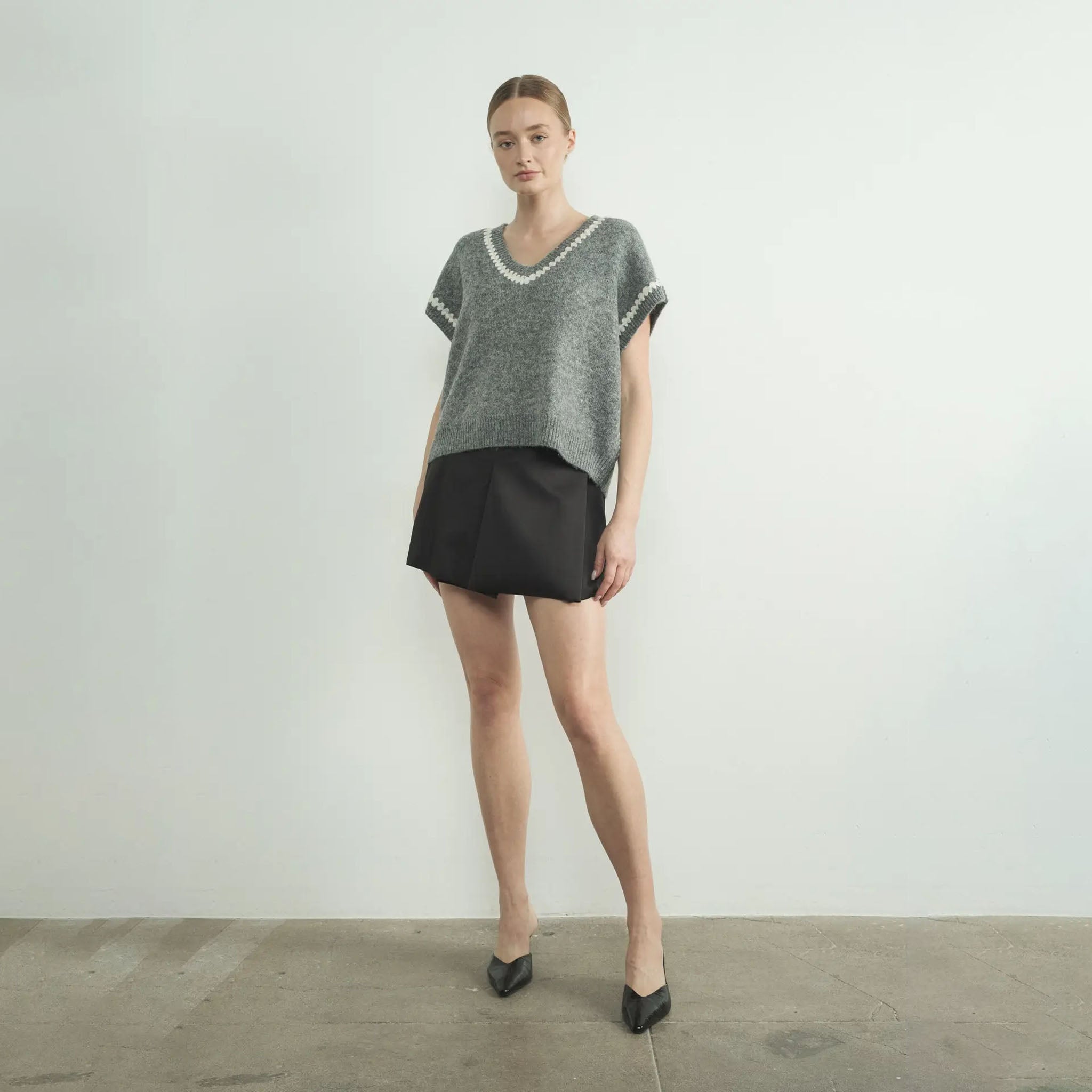 Woman wearing gray Aaron and Amber grey sweater vest and black skirt against a plain background