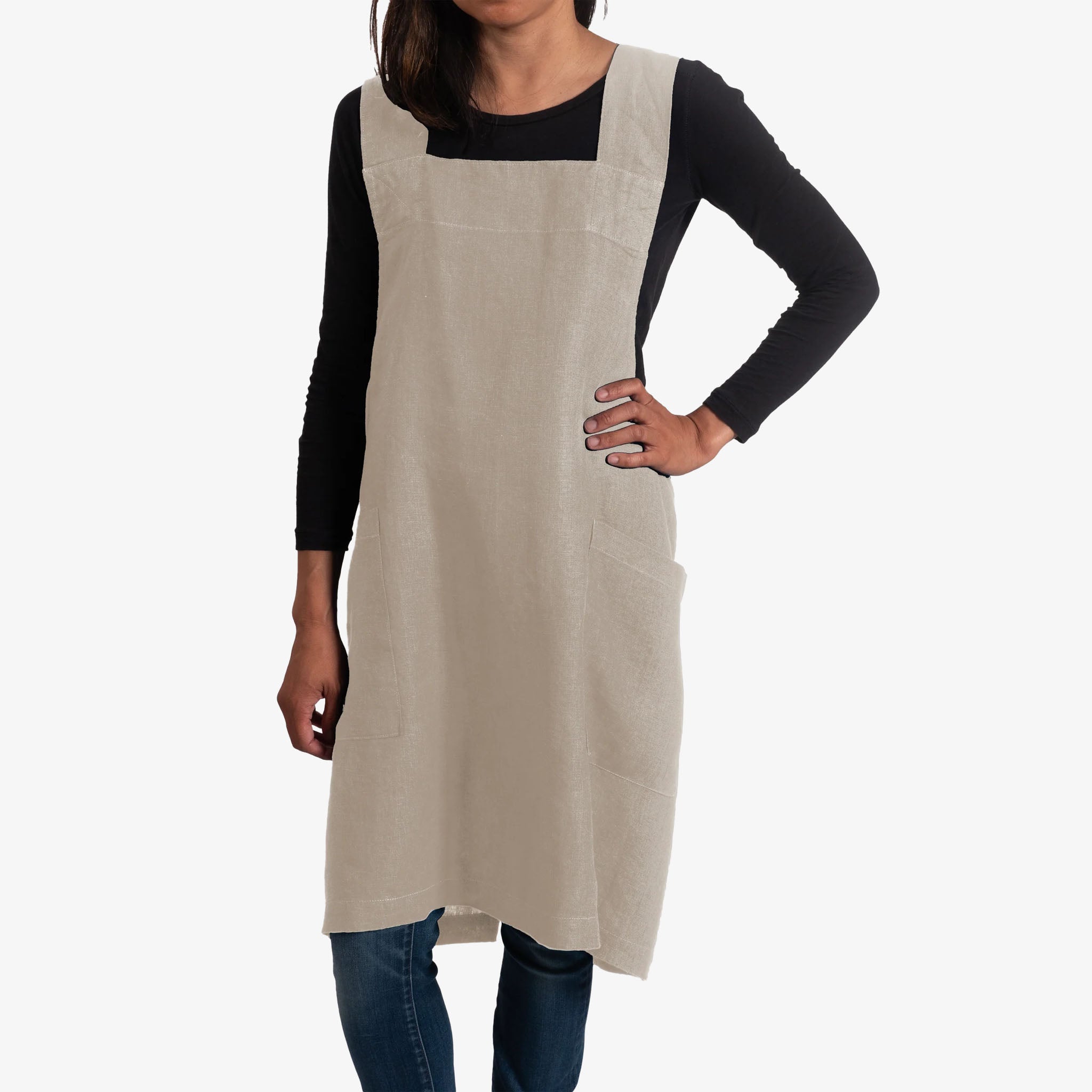 Person wearing a beige apron over a black long-sleeve shirt on a white background