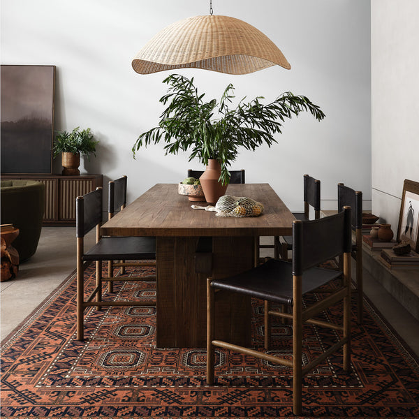 Four Hands Kena Dining Chairs in Sonoma Black around a dining table in space with dark wood and rattan light fixture