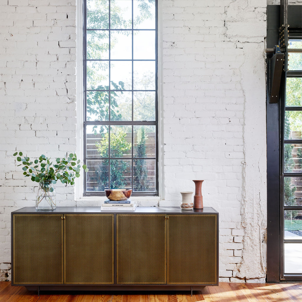 Four Hands Hendrick Sideboard with four perforated brass doors and gunmetal exterior in a loft space with white brick walls black frame mullioned windows