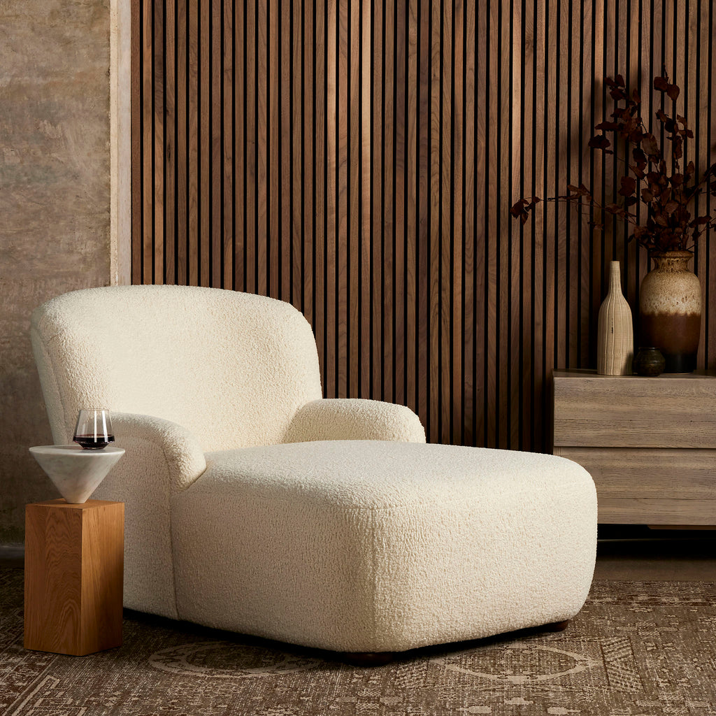 Four Hands Kadon Chaise Lounge In Natural Sheepskin in a wood panelled room with neutral rug and furniture
