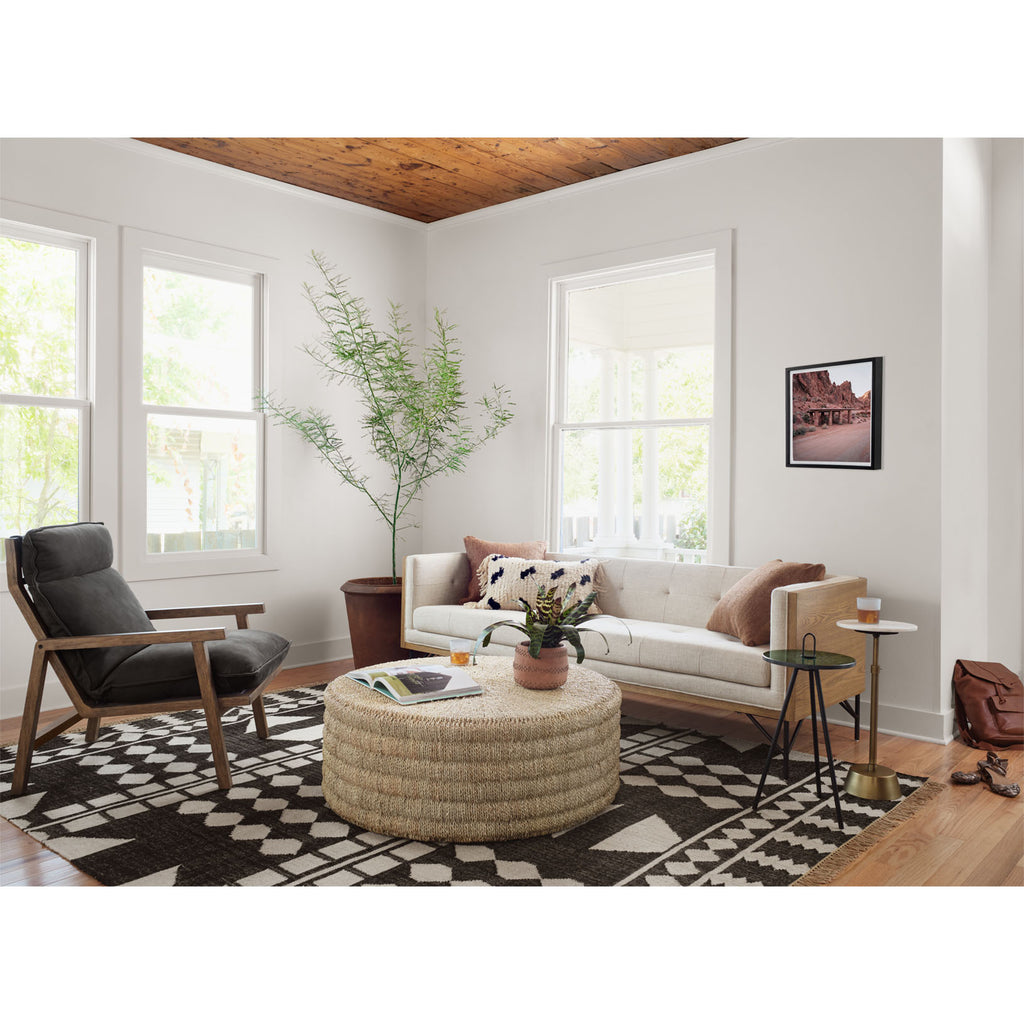 Living room with Four Hands Pascal Natural woven seagrass style Coffee Table on black and white rug with beige sofae and black side chair