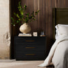Black Suki nightstand with 3 drawers and brass hardware made by Four Hands Furniture in a bedroom with reeded wood walls