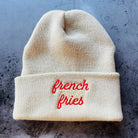 Beige beanie with 'french fries' embroidered in red on a textured surface