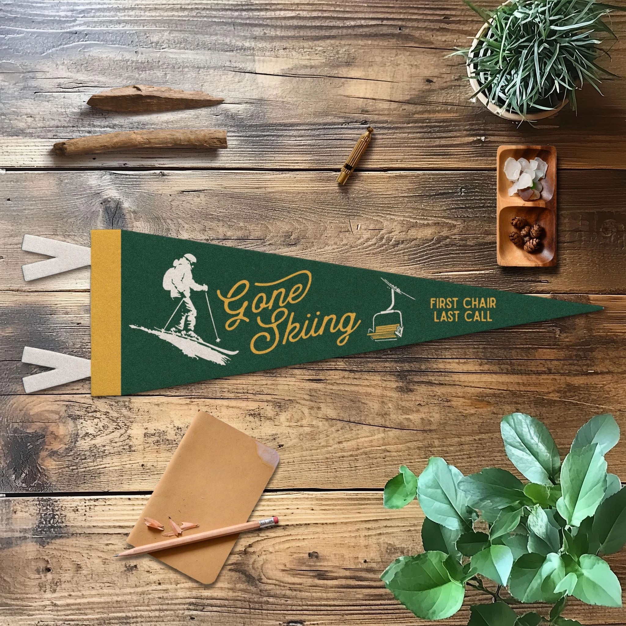 Green felt pennant with saying 'Gone Skiing First Chair last call' on a wood table 