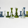 Collection of green, blue and clear glass candlesticks on a white background