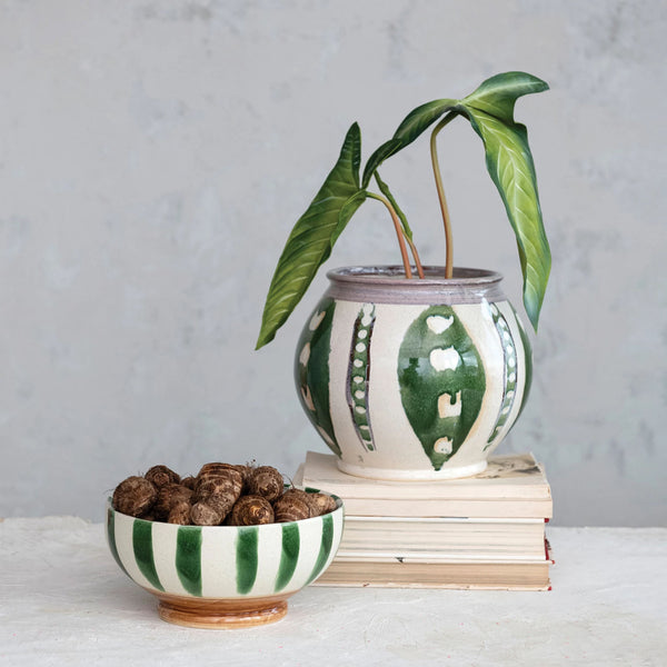 Green and white hand painted planter on top of s tack of books next to green and white painted bowl on a white counter