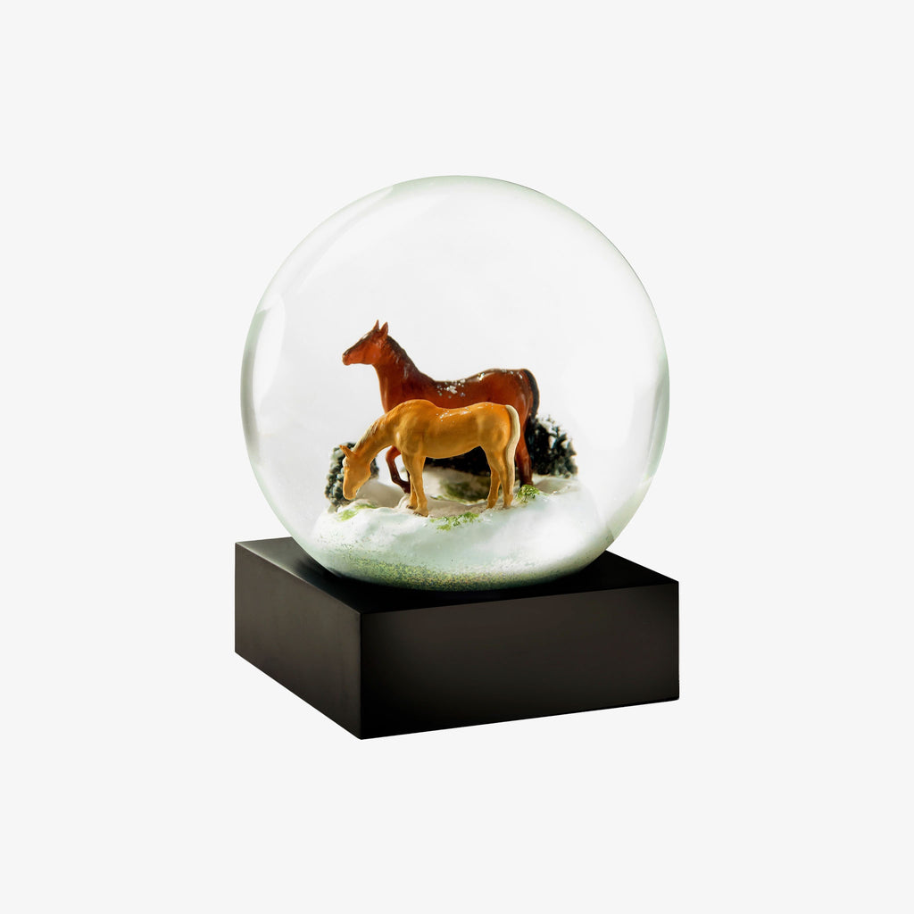 Snow Globe with two horses in snow with greenery on a white background
