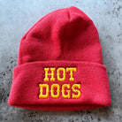 Red beanie with 'HOT DOGS' in yellow on a gray surface