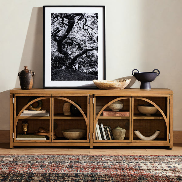Four Hands Ilana Media Console with glass front and arched wood accent  in living space with tribal rug 